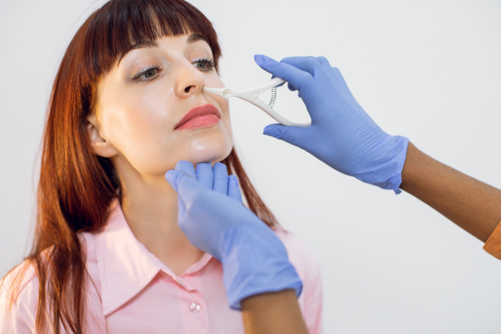 Close up of face of young red haired girl during medical examination in the ENT office. Hands of